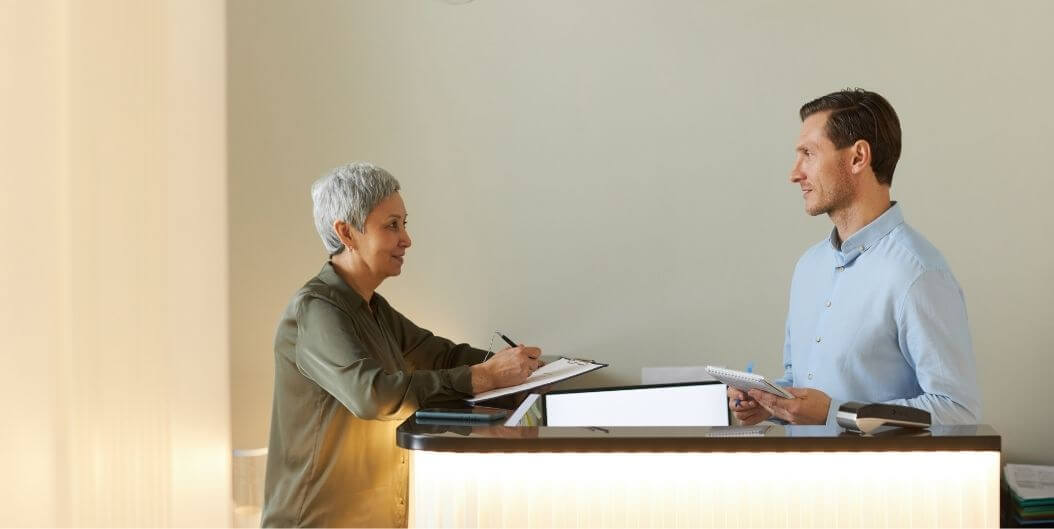 Senior Woman Speaking With Male Concierge Staff At Independent Living Facility