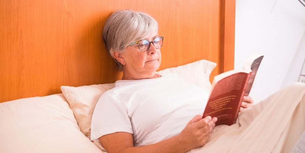 Senior Woman Reading Book in Private Bedroom at Independent Living Facility