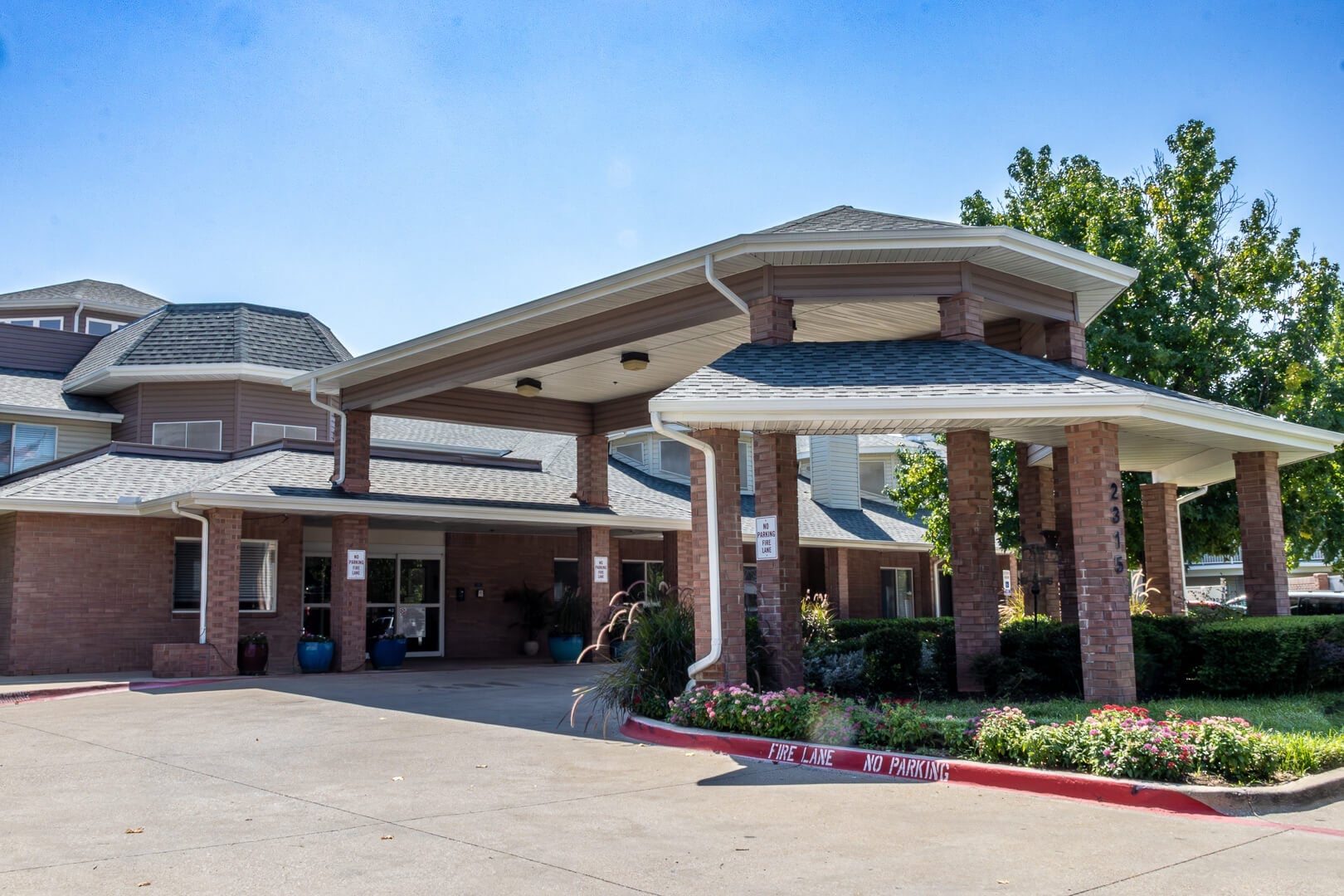 Covered Brick Entrance with Landscaped Driveway and Flowers at Our Independent Living Community